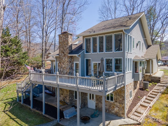 rear view of house featuring a patio, stone siding, a chimney, and stairs