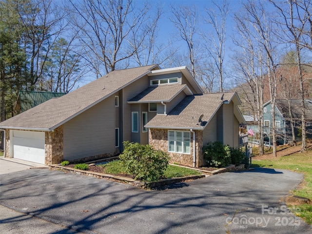 view of side of property featuring an attached garage, a shingled roof, stone siding, and driveway