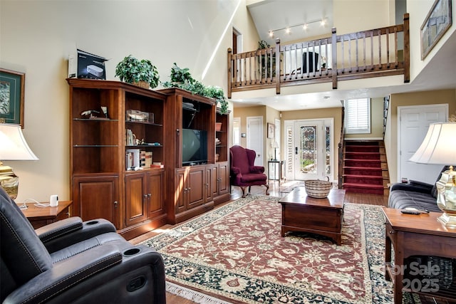 living area featuring a high ceiling, wood finished floors, rail lighting, and stairs