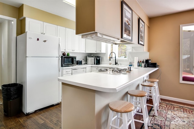 kitchen with dark wood-style flooring, white appliances, a peninsula, white cabinets, and a breakfast bar area