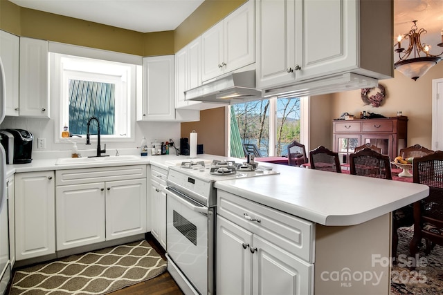 kitchen with electric range, a peninsula, a chandelier, under cabinet range hood, and a sink