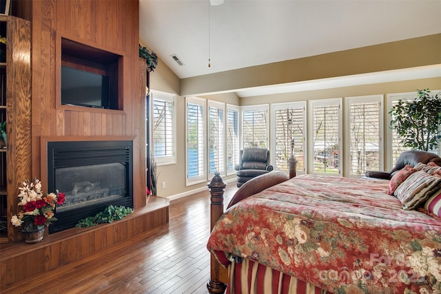 bedroom with wood finished floors, a glass covered fireplace, lofted ceiling, and visible vents