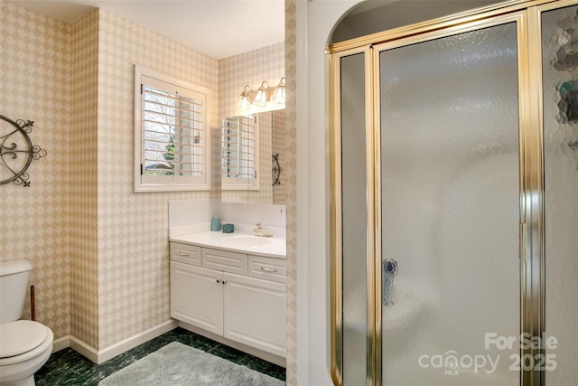 bathroom with a shower stall, vanity, toilet, wallpapered walls, and baseboards