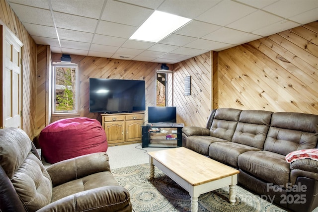living room featuring wood walls, carpet, and a drop ceiling