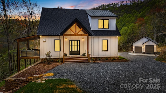 modern inspired farmhouse with covered porch, an outdoor structure, a detached garage, board and batten siding, and a shingled roof