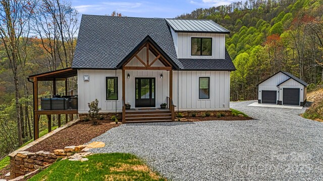 modern farmhouse style home featuring a garage, board and batten siding, an outdoor structure, a porch, and roof with shingles