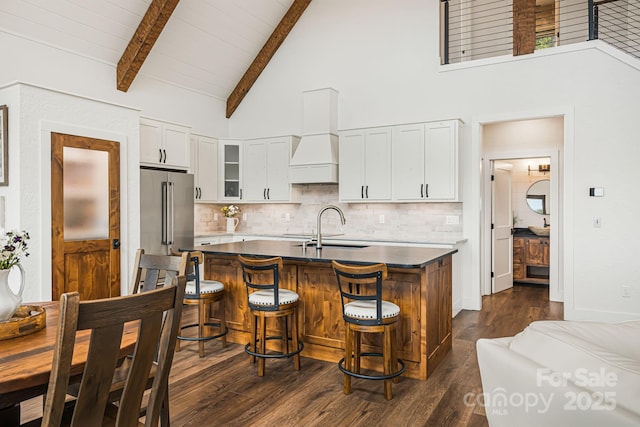 kitchen with a sink, tasteful backsplash, beam ceiling, a kitchen island with sink, and glass insert cabinets