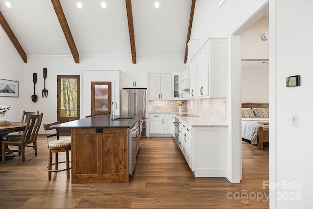 kitchen featuring dark wood-style flooring, a sink, backsplash, white cabinets, and an island with sink