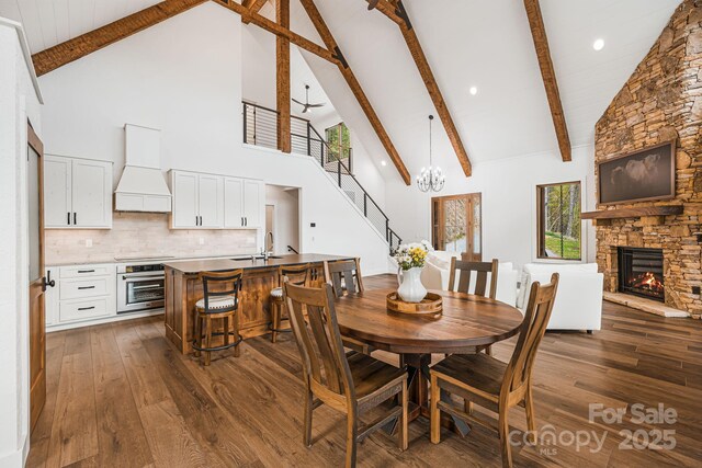 dining room with high vaulted ceiling, a fireplace, dark wood-type flooring, beamed ceiling, and stairs