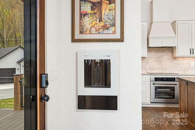 interior details featuring backsplash, stainless steel oven, custom exhaust hood, and a textured wall