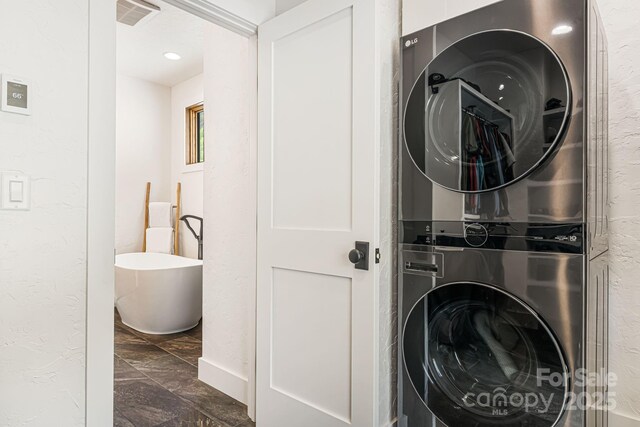 washroom featuring marble finish floor, laundry area, stacked washer / drying machine, visible vents, and a textured wall