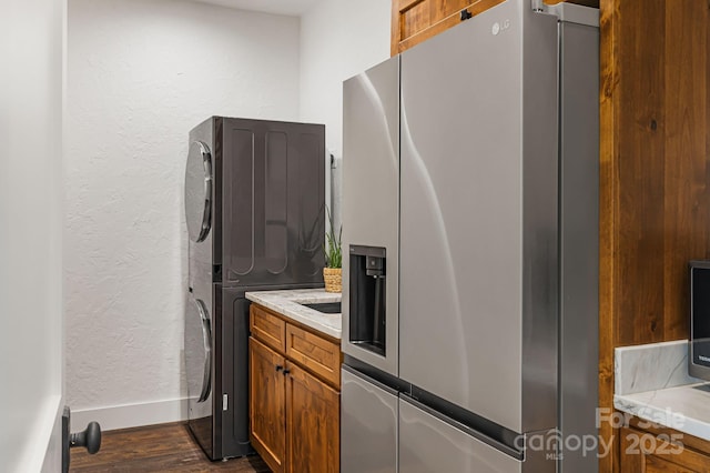 kitchen featuring baseboards, light countertops, dark wood-style floors, stacked washing maching and dryer, and stainless steel fridge with ice dispenser