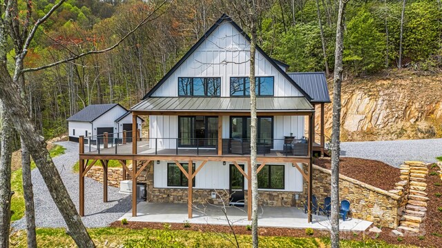 back of house with stone siding, a patio, and a view of trees