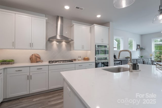 kitchen featuring a sink, stainless steel appliances, visible vents, white cabinetry, and wall chimney range hood