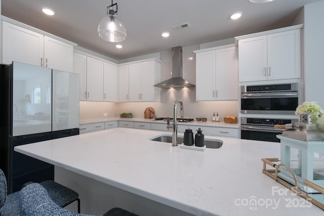 kitchen featuring stainless steel double oven, a kitchen bar, wall chimney exhaust hood, visible vents, and freestanding refrigerator