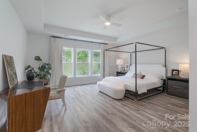 bedroom with a raised ceiling, wood finished floors, and ceiling fan