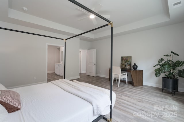 bedroom with baseboards, visible vents, wood finished floors, and a tray ceiling