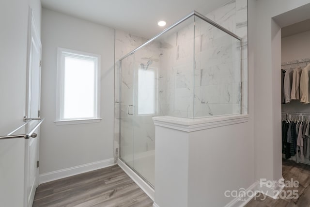 full bath featuring wood finished floors, baseboards, a marble finish shower, and a walk in closet