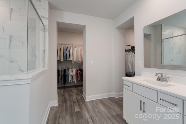 bathroom with vanity, baseboards, wood finished floors, a spacious closet, and tiled shower