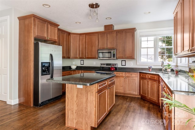 kitchen featuring stainless steel appliances, a sink, dark wood-type flooring, a center island, and brown cabinetry