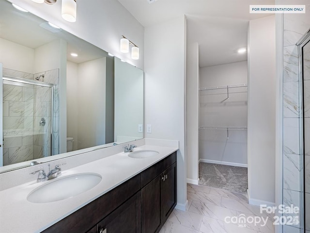 full bathroom featuring a walk in closet, a shower stall, marble finish floor, and a sink