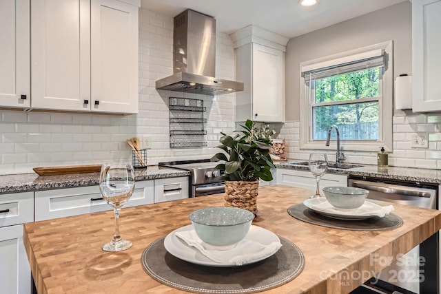 kitchen with butcher block countertops, a sink, white cabinetry, wall chimney exhaust hood, and appliances with stainless steel finishes