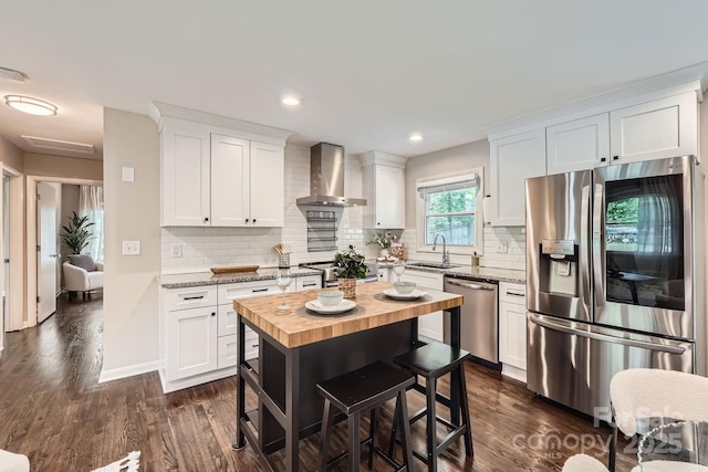 kitchen with white cabinets, stainless steel appliances, a sink, wall chimney exhaust hood, and wood counters