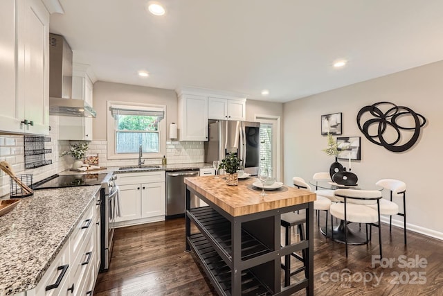 kitchen featuring wall chimney range hood, decorative backsplash, appliances with stainless steel finishes, and white cabinetry