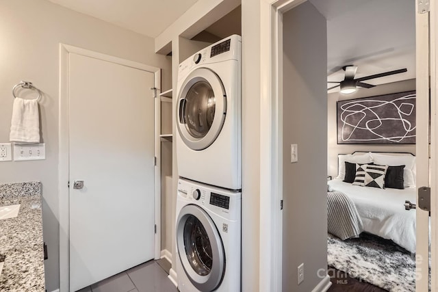 laundry area with tile patterned flooring, ceiling fan, stacked washer / dryer, and laundry area