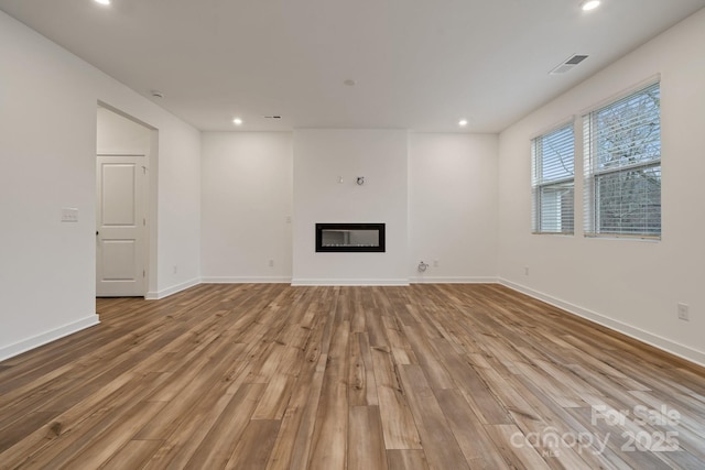 unfurnished living room with a glass covered fireplace, recessed lighting, visible vents, and wood finished floors