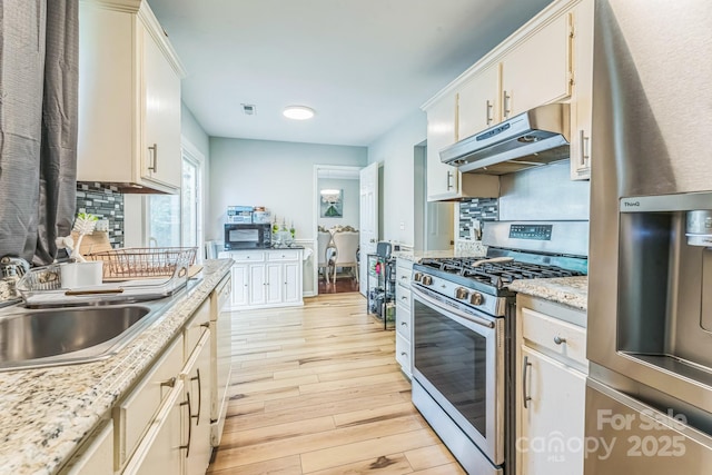 kitchen with stainless steel range with gas cooktop, black microwave, refrigerator, under cabinet range hood, and a sink