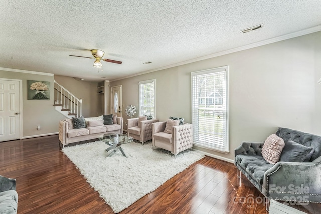 living room with dark wood-type flooring, a textured ceiling, ornamental molding, visible vents, and stairs