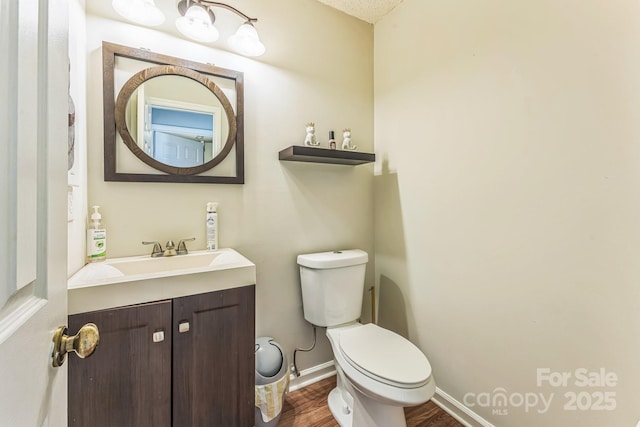 half bath featuring toilet, wood finished floors, vanity, and baseboards