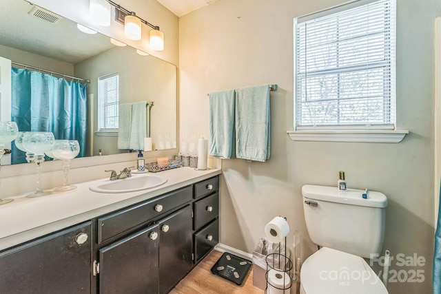 bathroom with visible vents, baseboards, toilet, vanity, and wood finished floors