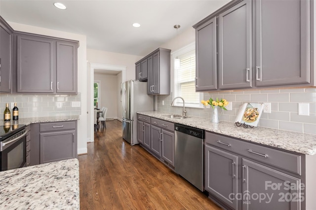 kitchen with stainless steel appliances, a sink, dark wood finished floors, light stone countertops, and decorative backsplash