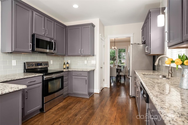 kitchen featuring stainless steel appliances, a sink, decorative backsplash, dark wood-style flooring, and light stone counters