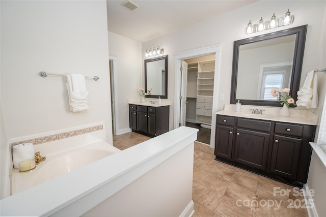 full bath with two vanities, a spacious closet, a bath, and tile patterned flooring