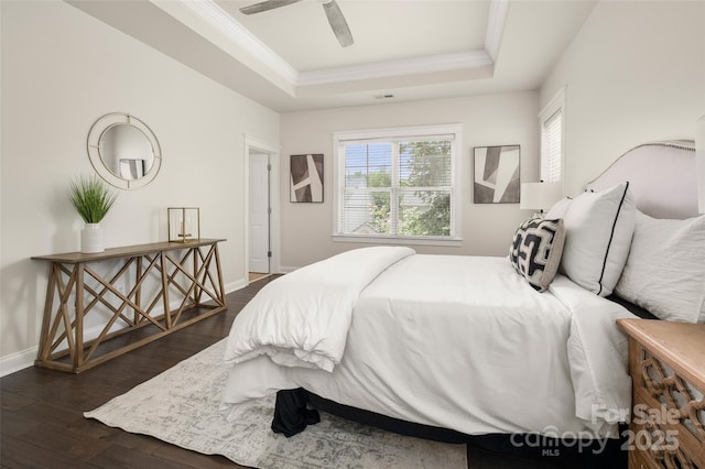 bedroom featuring a tray ceiling, crown molding, dark wood-style floors, baseboards, and ceiling fan