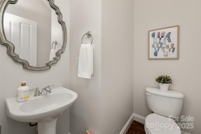 half bath with toilet, baseboards, wood finished floors, and a sink