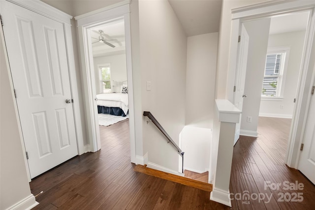hallway with an upstairs landing, dark wood-style floors, and baseboards