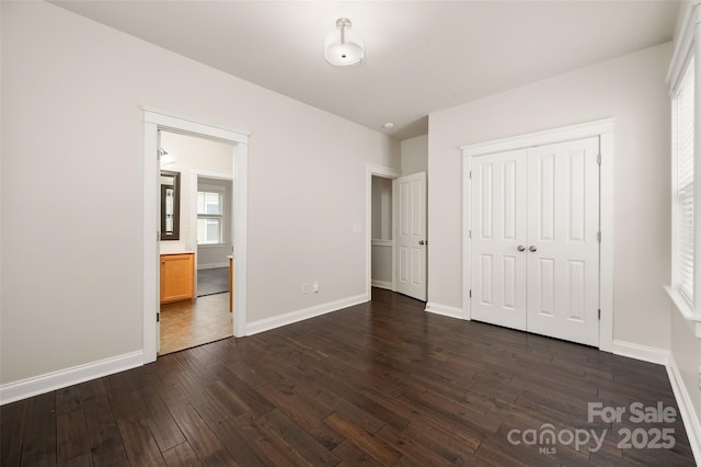 unfurnished bedroom with dark wood-style flooring, baseboards, a closet, and ensuite bathroom