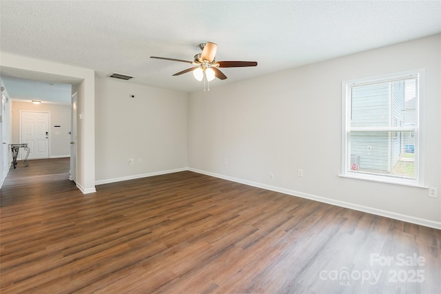 empty room featuring dark wood-style flooring, visible vents, baseboards, and a ceiling fan