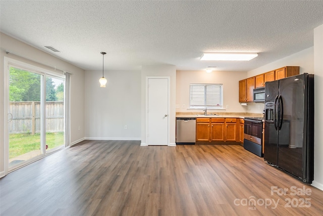 kitchen featuring a textured ceiling, black appliances, wood finished floors, light countertops, and a sink
