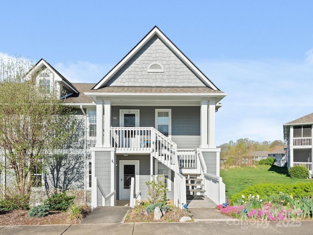 view of front of home featuring a shingled roof, covered porch, and stairs
