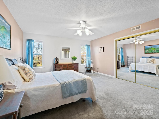 carpeted bedroom with a textured ceiling, multiple windows, and visible vents