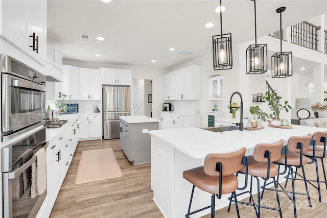 kitchen featuring a sink, stainless steel appliances, light wood finished floors, a center island with sink, and visible vents