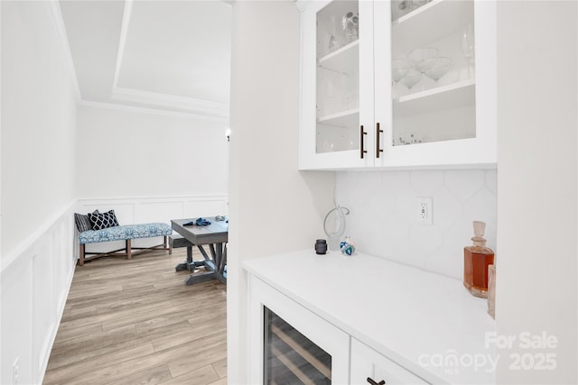 bar featuring a decorative wall, crown molding, beverage cooler, a wainscoted wall, and light wood-style flooring