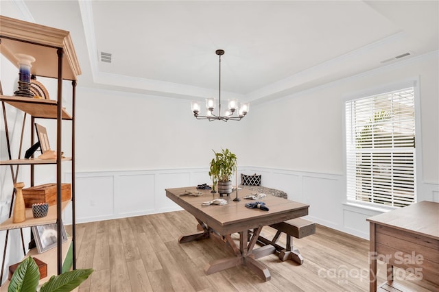 dining space with a tray ceiling, light wood-style flooring, visible vents, and an inviting chandelier