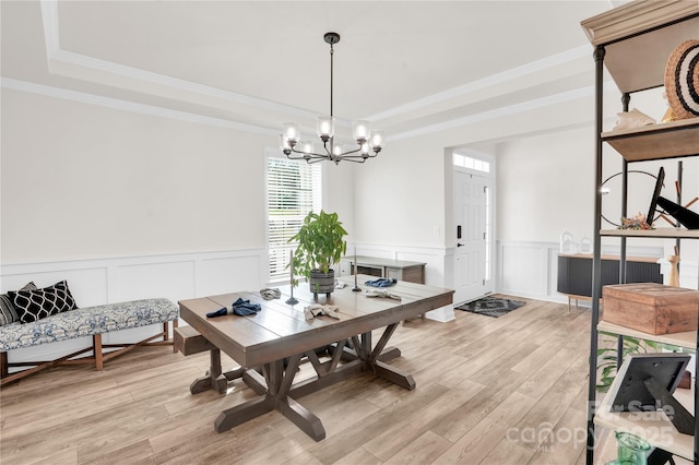 dining space with a tray ceiling, a chandelier, light wood-style floors, and a decorative wall