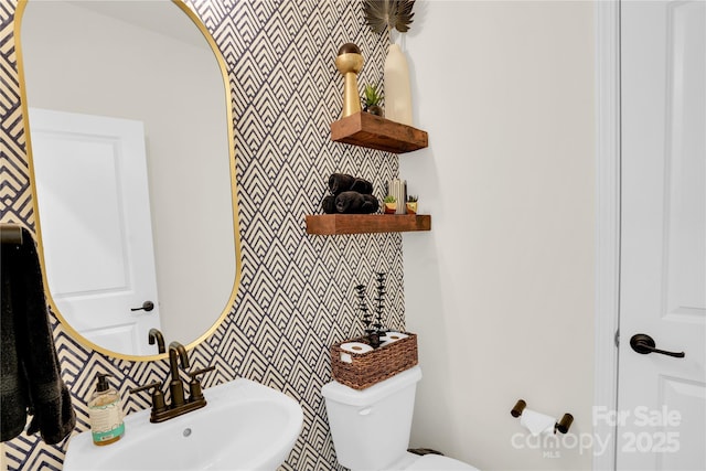half bath featuring toilet, a sink, and wallpapered walls